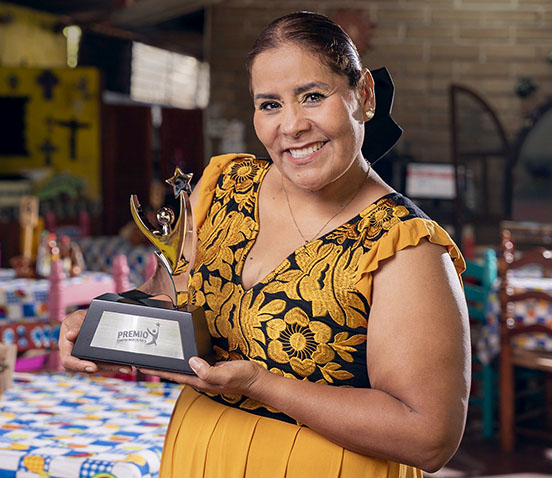 Yadira Tziu ganadora del Premio Emprendedores 2024, con trofeo en su taller de costura.
